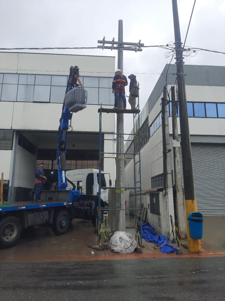 Equipe trabalhando na instalação elétrica em poste com caminhão de apoio