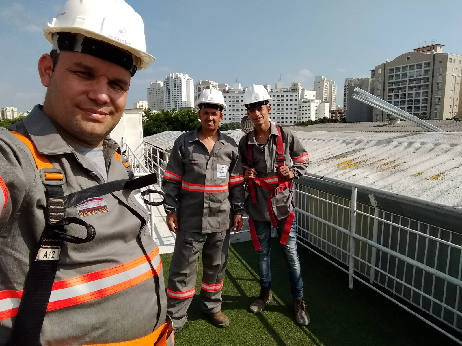 Três profissionais com capacetes e equipamentos de segurança durante trabalho em uma cobertura